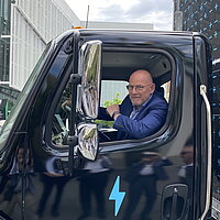 Verkehrsminister Winfried Hermann sitzt in einem elektrischen Lkw und schaut aus dem Fenster