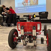 Nahaufnahme und Rückansicht eines Elektro-Karts; im Hintergrund baut eine Gruppe Jugendlicher ein Elektro-Kart zusammen.