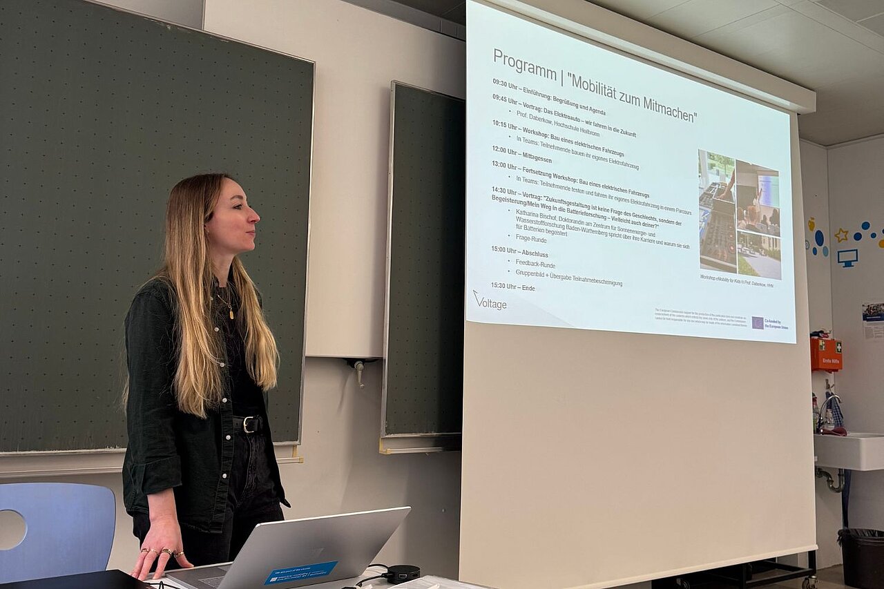 Eine Frau steht vor einer Leinwand und stellt das Programm des Battery Camps vor.