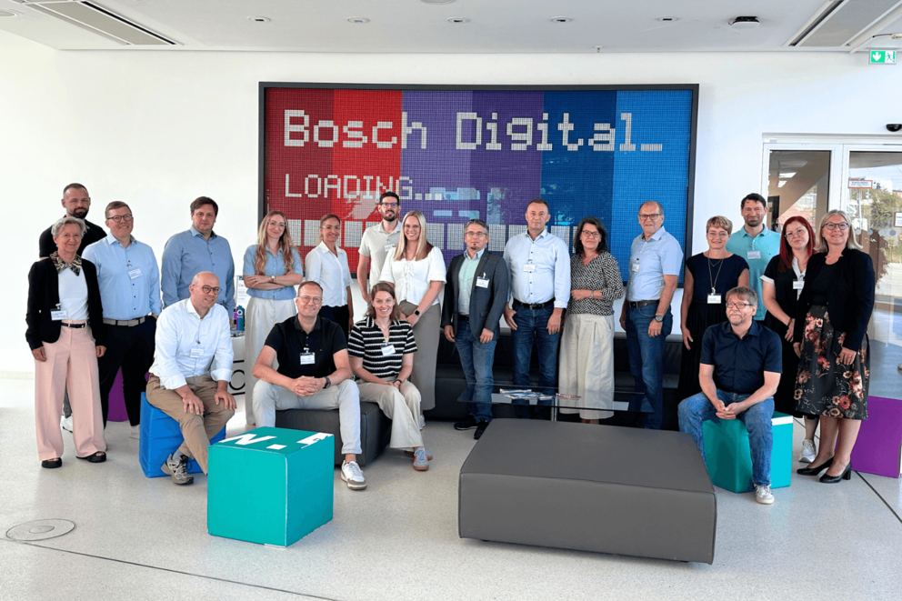 Eine Gruppe von Personen steht vor einem digitalen Schild des Unternehmens Bosch und lächelt in die Kamera.