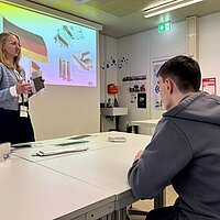 Eine Frau präsentiert ihren Karriereweg in der Batterieindustrie; ein Junge hört aufmerksam zu.