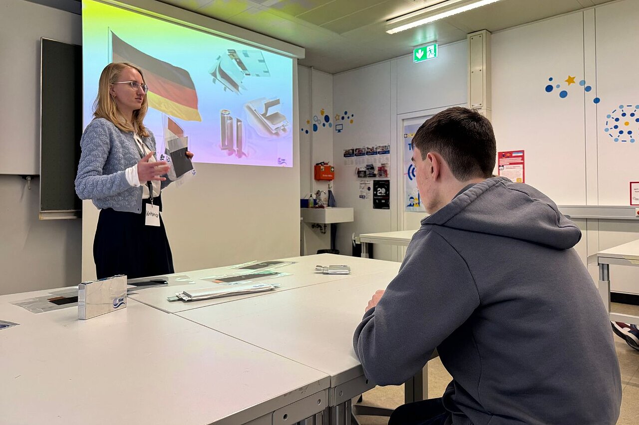 Eine Frau präsentiert ihren Karriereweg in der Batterieindustrie; ein Junge hört aufmerksam zu.