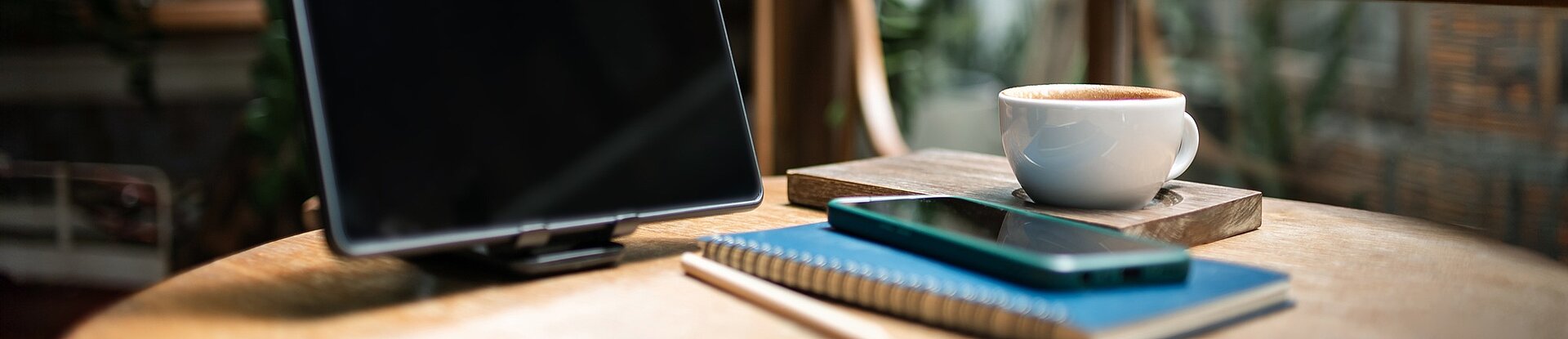 Auf einem runden Tisch stehen ein Bildschirm, mehrere Bücher und eine Kaffeetasse.