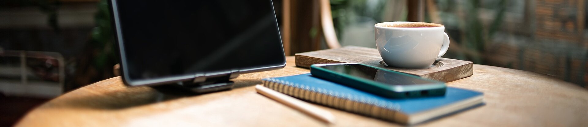 Arbeitsplatz Auf einem runden Tisch stehen ein Bildschirm, mehrere Bücher und eine Kaffeetasse.