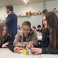 Drei Mädchen sitzen an einem Tisch und bauen gemeinsam eine modellhafte Batteriezelle aus Kunststoff zusammen.