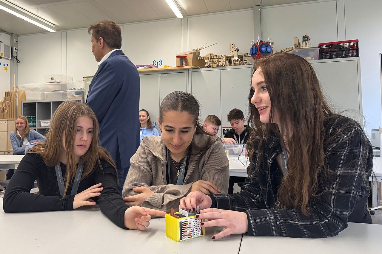 Drei Mädchen sitzen an einem Tisch und bauen gemeinsam eine modellhafte Batteriezelle aus Kunststoff zusammen.