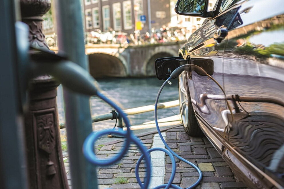 Ein E-Auto beim Laden an einer Ladesäule in der Stadt am Ufer eines Gewässers.