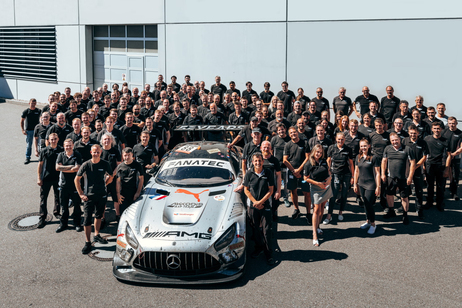 En Gruppenfoto der HWA AG, auf dem mehrere Mitarbeiter: innen zu sehen sind. Ein Fahrzeug ist in der Mitte platziert.