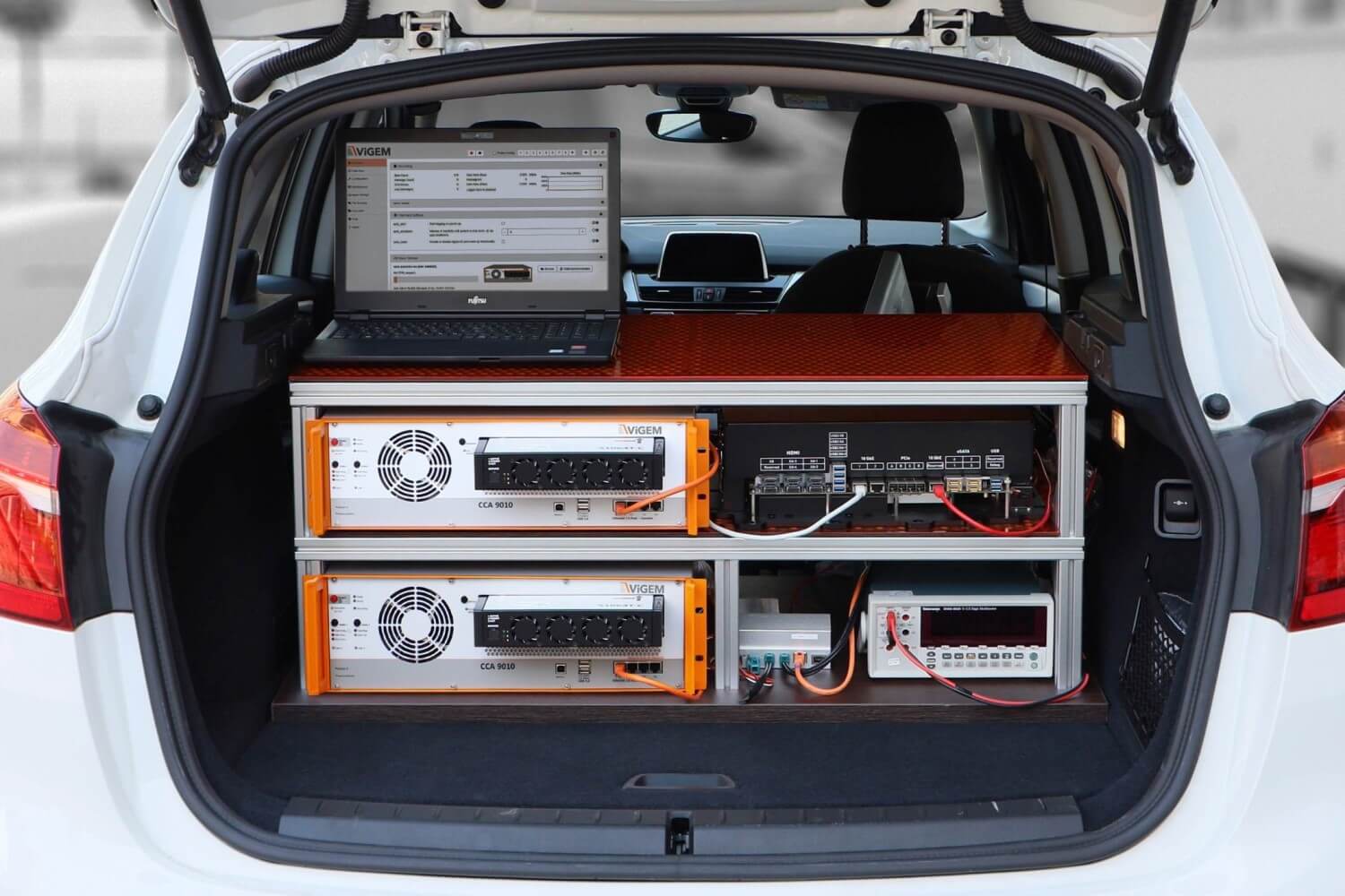 Das Bild zeigt den Kofferraum eines weißen Fahrzeugs, das mit verschiedenen elektronischen Geräten ausgestattet ist.