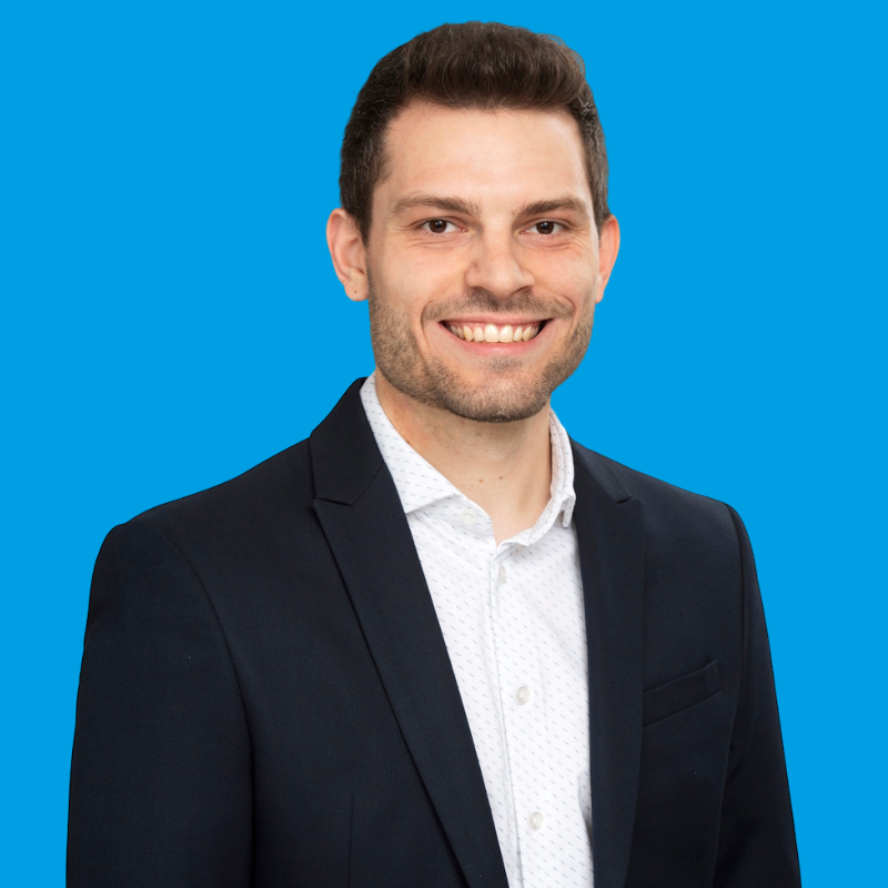 Porträt von Benjamin Kleiner vor einem blauem Hintergrund.